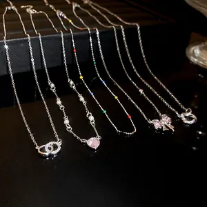 Détail de colliers en zircon avec pendentifs cœur, nœud et cercle sur surface noire.