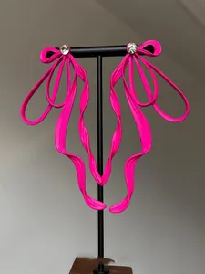 Detailed macro view of oversized neon pink rhinestone bow earrings on a black display stand