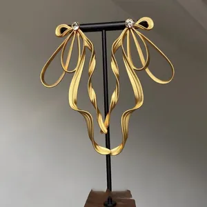 Detailed view of oversized golden ribbon bow earrings with a central sparkling rhinestone