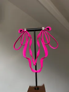 Close-up of bright pink ribbon bow earrings with sparkling crystal stud on a stand