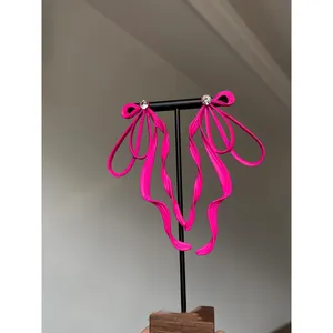 Detailed view of fluorescent pink ribbon bow earrings with rhinestone studs