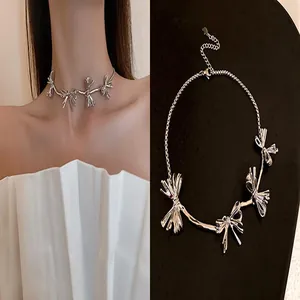 Close-up of silver bow choker necklace on model and black display stand.