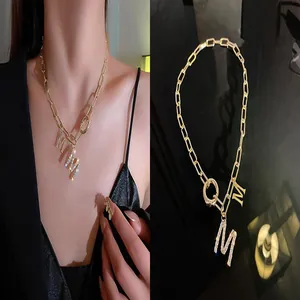 Macro view of gold chain necklace featuring sparkling rhinestone-paved M letter pendants