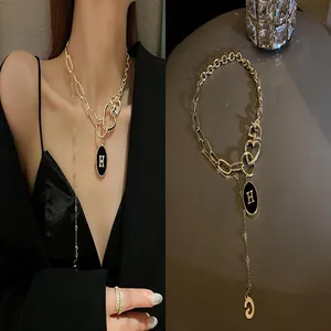 Detailed view of gold chain necklace with black 'H' pendant and layered thin chain
