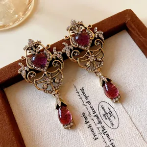 Detailed view of vintage gold earrings with purple heart stones and red teardrop drops