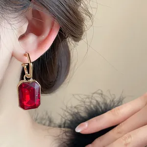 Elegant vintage style gold drop earrings with a faceted red rectangular gemstone on model