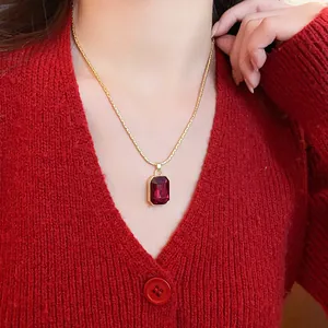 Macro view of a red emerald-cut gemstone pendant on a gold chain worn with a red sweater
