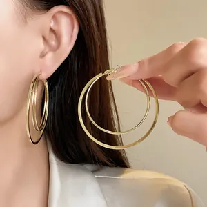 Detailed close-up view of large gold multi-layer hoop earrings shown on ear and held by hand