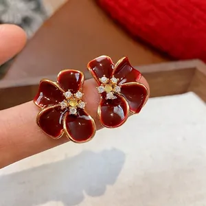 Elegant gold plated zircon flower stud earrings in Ankara red on finger display