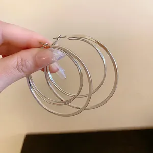 Close-up of silver multi-layer oversized hoop earrings held by hand for a detailed view.