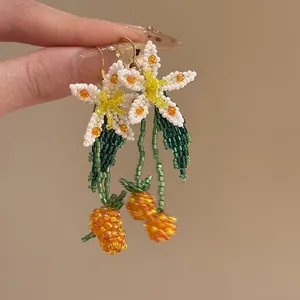 Close-up of handmade beaded tassel earrings with white flowers and orange fruit dangles.