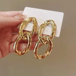 Close-up of golden irregular oval link earrings on a white display card held by hand.