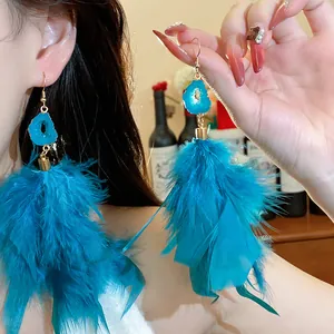 Hand holding blue feather dangle earrings with geode drop detail