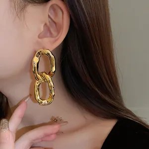 Close-up detail of stylish gold irregular oval link drop earrings worn by a model