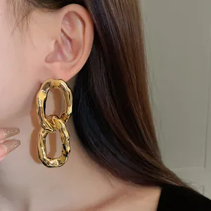Close-up detail view of golden irregular chunky oval link earrings worn by a model