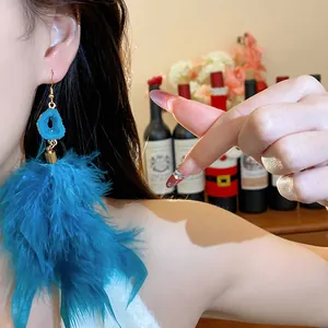 Detailed view of oversized turquoise feather tassel earrings with blue stone accent