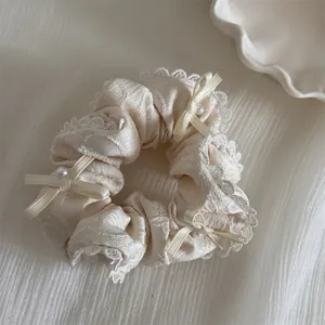 Nahaufnahme eines cremefarbenen Spitzen-Scrunchies mit Schleifen und Perlen.
