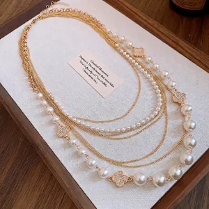 Elegante mehrlagige Goldkette mit weißen Perlen und kristallbesetzten Kleeblatt-Anhängern