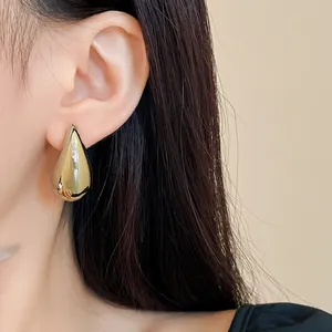 Nahaufnahme eines minimalistischen goldenen Wassertropfen-Ohrsteckers am Ohr einer Frau