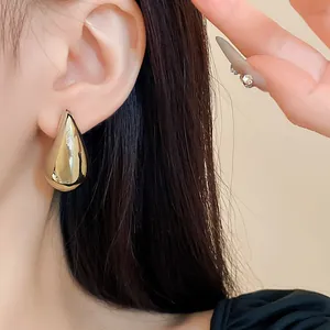 Nahaufnahme eleganter goldener Tropfenohrringe am Ohr, die ein poliertes Finish zeigen
