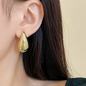 Detailaufnahme eines großen goldenen Metall-Tropfenohrsteckers, der am Ohr getragen wird