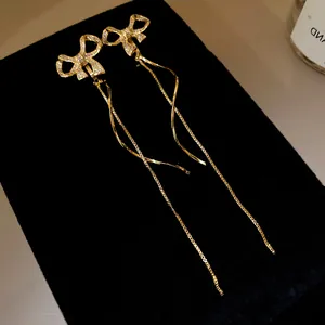 Detail von 18k vergoldeten Schleifenohrringen mit langen Quasten und funkelnden Zirkoniasteinen.