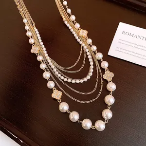 Detailansicht einer eleganten mehrlagigen Goldhalskette mit Perlen und Kleeblatt-Anhängern.