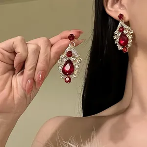 Detailed close-up of vintage red zircon waterdrop earrings on model's ear and hand.