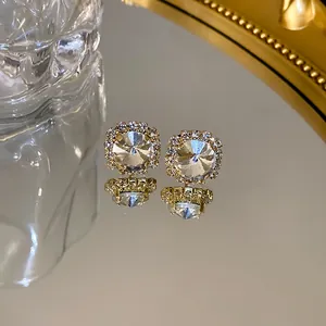 Close-up of elegant square gold stud earrings with sparkling crystals reflected on a mirror surface