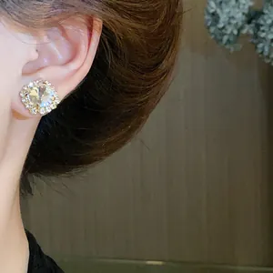 Close-up detail of elegant square crystal stud earrings worn on a model's ear lobe