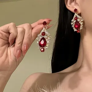 Detailed view of ornate red teardrop earrings with sparkling crystals on a model