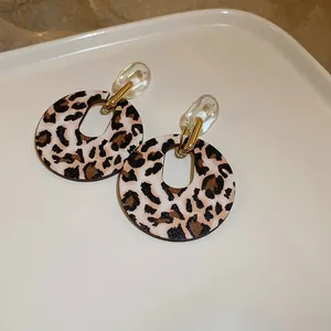 Detalle de pendientes geométricos vintage con estampado de leopardo y cadena.
