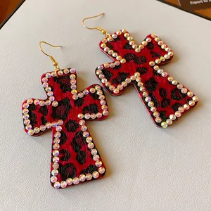 Vista detallada de pendientes de cruz con estampado de leopardo rojo y bordes de cristal.