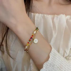 Detailed view of colorful beaded pearl bracelet and gold chain with daisy charm