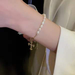 Close-up of elegant pearl bracelet with golden gothic cross pendant on model wrist