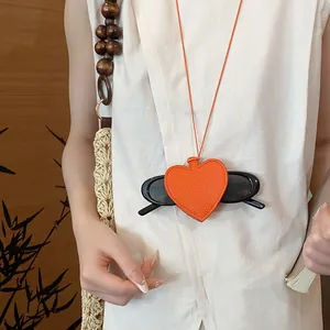 Detail view of orange leather heart pendant necklace holding black sunglasses.