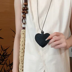 Close-up of a heart-shaped black pebbled leather sunglass storage pouch worn as a necklace