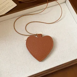 Detail view of brown heart-shaped leather pendant with textured finish on brown cord.