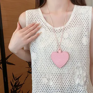 Detailed view of a pink heart-shaped leather pendant necklace worn on a white lace top
