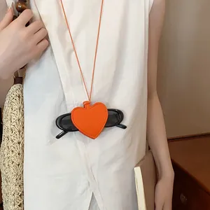 Orange heart-shaped leather necklace holding black sunglasses in a lifestyle shot