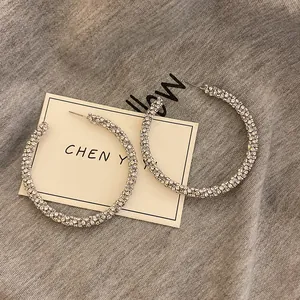 Close-up detail of oversized silver needle hoop earrings fully paved with sparkling rhinestones