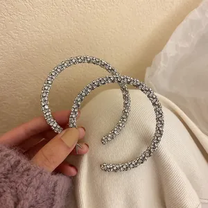 Close-up of large silver hoop earrings fully pavé set with sparkling rhinestones.
