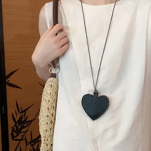 Close-up of black leather heart pendant necklace worn as stylish sunglasses storage bag.
