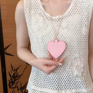 Close-up of pink litchi grain leather heart pendant with cord on white lace fabric.