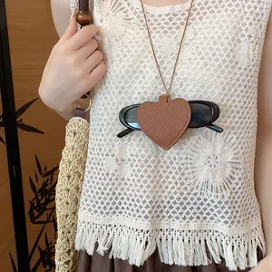 Close-up detail of a heart-shaped brown leather sunglasses holder worn as a necklace