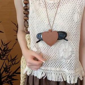 Close-up of a brown leather heart-shaped sunglasses holder necklace on a lace top.