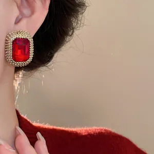 Dettaglio macro di un orecchino vintage rettangolare rosso con bordo dorato testurizzato.