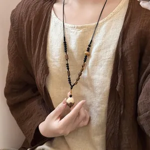 Detailopname van een Zen-stijl bloemenhanger aan een ketting op linnen kleding.
