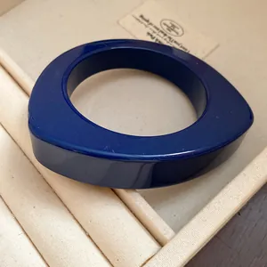 Dettaglio di un bracciale rigido in resina blu scuro con un design asimmetrico.