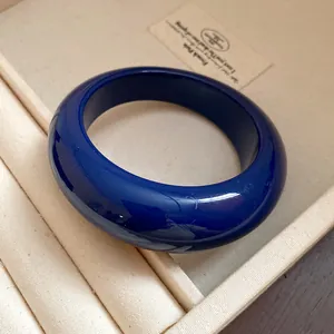 Primo piano di un bracciale rigido in resina blu scuro lucida in scatola beige.